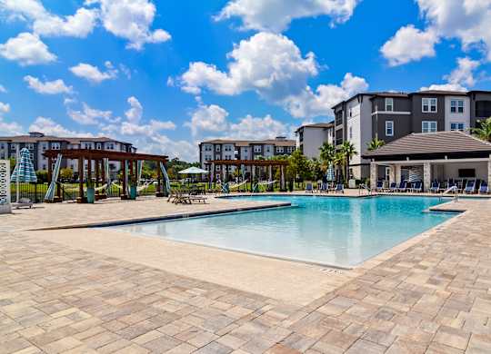 A large swimming pool surrounded by a brick patio and a resort-style building in the background.