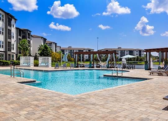 A large swimming pool surrounded by a tiled patio and lounge chairs.