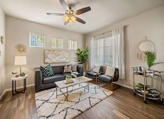 A living room with a grey couch, a coffee table, a ceiling fan, and a rug.