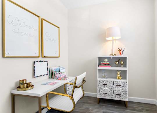 A white desk with a gold chair and a lamp on a grey shelf.