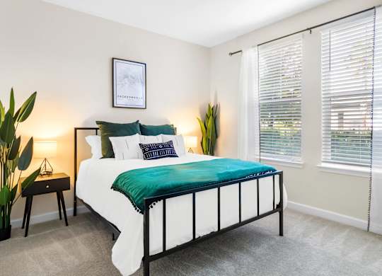 A bed with a green blanket and white pillows in a room with a window.