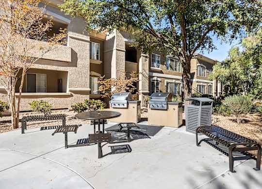 A patio with a table and chairs is surrounded by trees and a building.