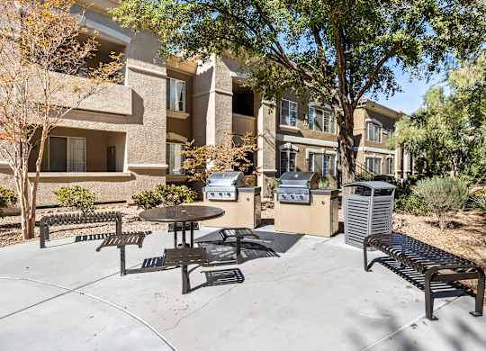 A patio with a table and chairs is surrounded by trees and apartment buildings.