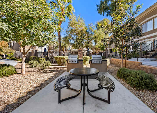 A table and chairs set in a courtyard with a tree and a building in the background.