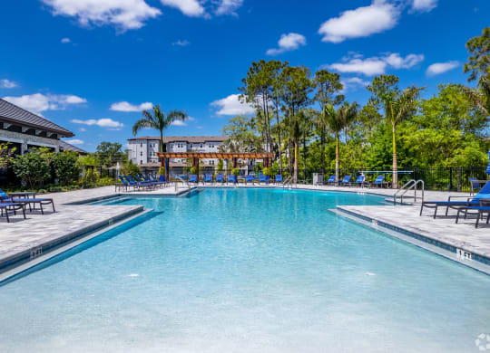 a large swimming pool with chaise lounge chairs and a building in the background at The Oasis at Manatee River, Bradenton, FL, 34211