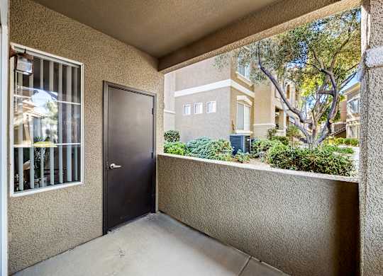 A balcony with a door and a window overlooking a building and trees.