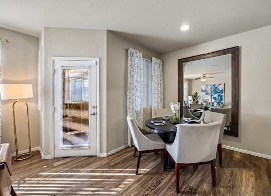 A dining room with a table set for two and a view of a door with blinds.
