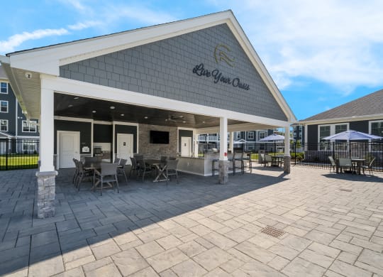 a covered patio with tables and chairs outside of a building at The Oasis at Plymouth, Plymouth, MA, 02360