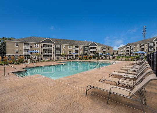 A swimming pool surrounded by sun loungers in front of apartment buildings.