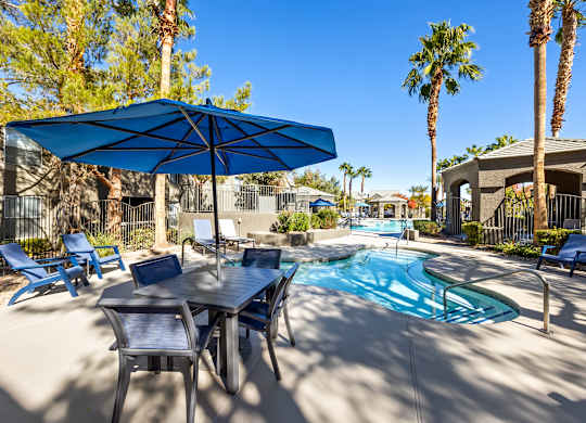 A pool area with a table and chairs and a blue umbrella.