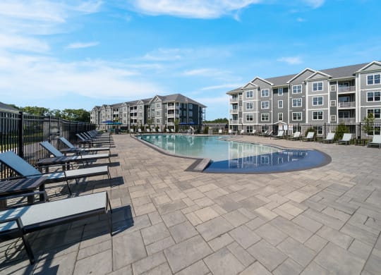 a swimming pool with lounge chairs around it in front of an apartment building at The Oasis at Plymouth, Plymouth, MA, 02360