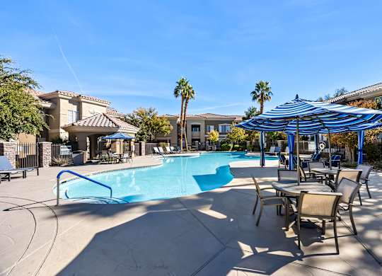 A swimming pool with a blue umbrella and chairs around it.