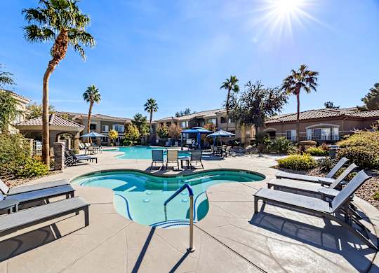 A sunny day at the pool with lounge chairs and palm trees.