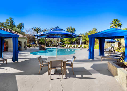 A pool area with a table and chairs under a blue canopy.