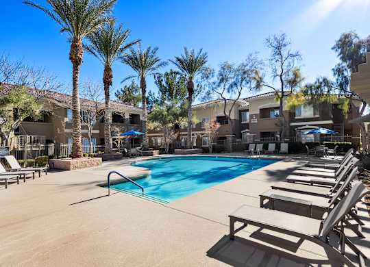 A pool surrounded by lounge chairs and palm trees.