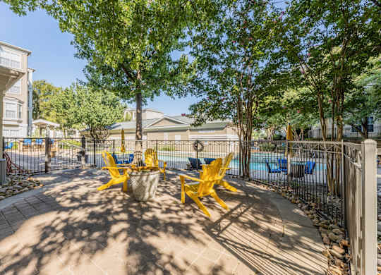 Small patio space with yellow chairs and a fence beside the swimming pool at Encore at Buckingham apartments in Richardson, TX