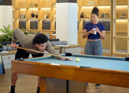 A man is playing pool while a woman stands nearby.
