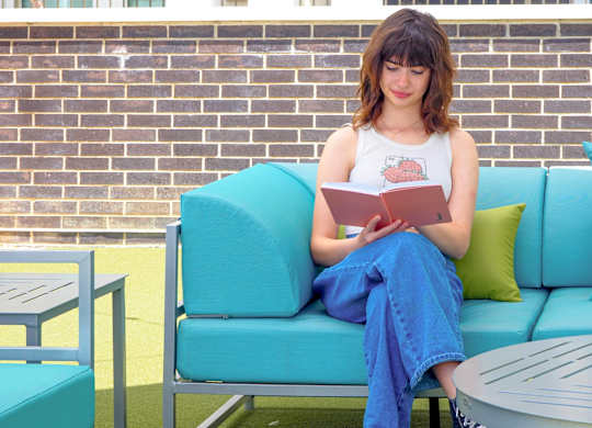 A woman is sitting on a blue couch reading a book.