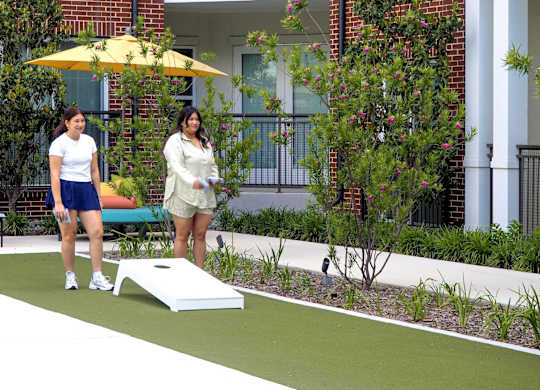 Two women playing cornhole in a garden.