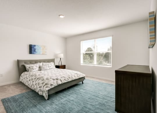 Furnished master bedroom with a bed, blue rug, dresser, and a window at Beacon at Arbours in Ruskin, FL