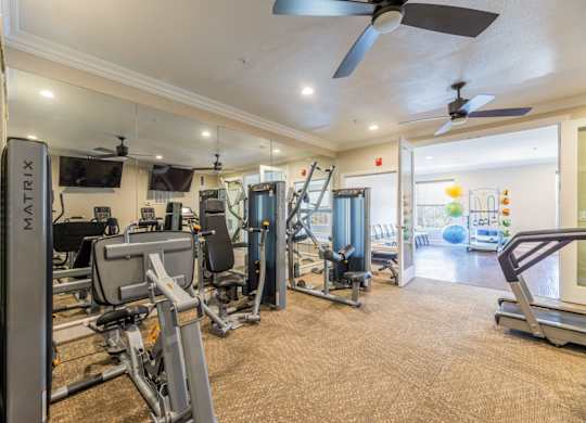 Cable machines including leg press, chest press, and lat pulldown machines in fitness center facing two tvs at Encore at Buckingham apartments in Richardson, TX