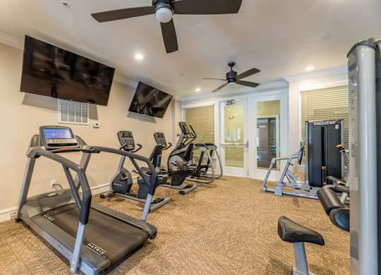 Cardio machines and cable weight equipment in the fitness center with ceiling fans and two TVs at Encore at Buckingham apartments in Richardson, TX
