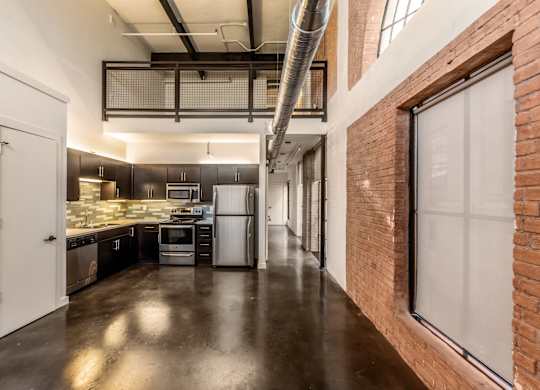 3333 Elm Street Lofts studio kitchen with stainless steel appliances, brick accent walls, and a large arched window at Deep Ellum Lofts in Dallas, TX