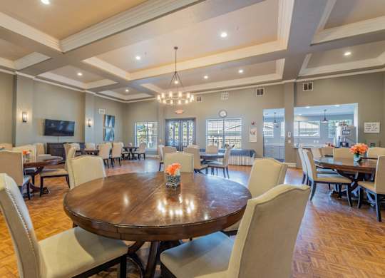 Grand ballroom with several tables and seating, a tv, and kitchen with a coffee maker machine at Encore at Buckingham apartments in Richardson, TX