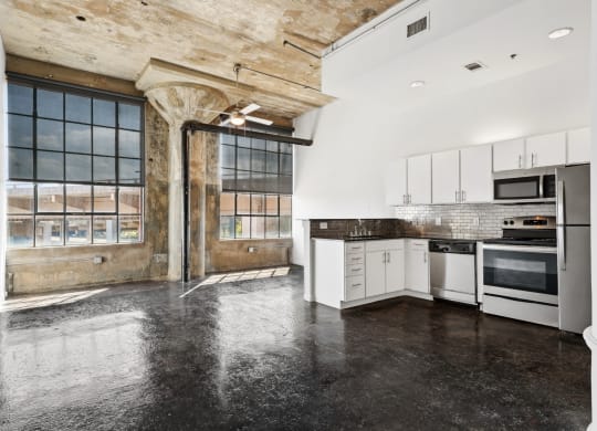 Loft kitchen and living space with stainless steel appliances, ceiling fan, and polished concrete floors | Adam Hats Lofts from Deep Ellum Lofts in Dallas, TX