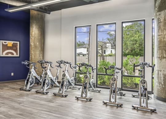 Spin bike area with large windows and mirrored wall at Allusion at West University apartments in Houston, TX