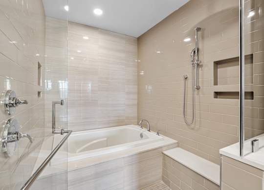 A modern bathroom with a walk-in glass shower and tub enclosure with tile walls at Alastair at Aria Village Apartments in Sandy Springs, GA