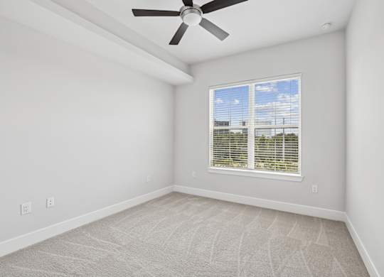 A carpeted bedroom from the C1 floorplan with a ceiling fan and a window with blinds at Alastair at Aria Village Apartments in Sandy Springs, GA