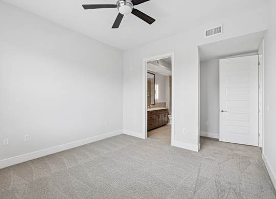 A carpeted bedroom from the C1 floorplan with a ceiling fan and connected bathroom at Alastair at Aria Village Apartments in Sandy Springs, GA