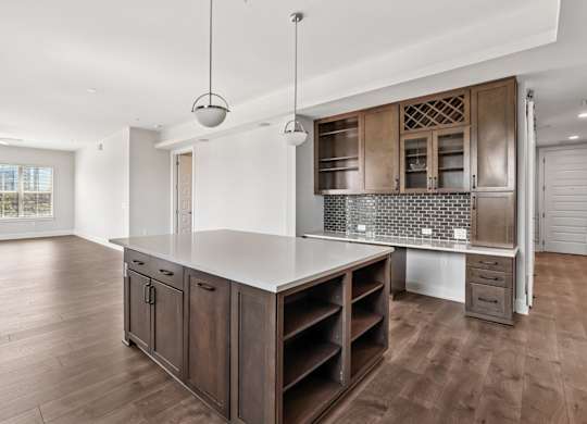 A modern kitchen from the C1 floorplan with a white countertop and island, brick backsplash, and wooden cabinets at Alastair at Aria Village Apartments in Sandy Springs, GA