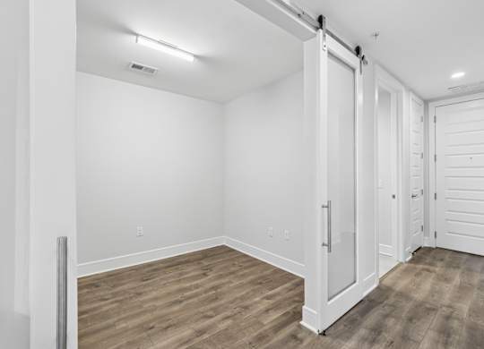 A study from the C1 floorplan with white walls, wooden flooring, and sliding barn doors at Alastair at Aria Village Apartments in Sandy Springs, GA