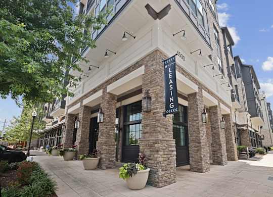 An exterior corner view of the leasing office at Alastair at Aria Village Apartments with a sign that says "Leasing" in front of it in Sandy Springs, GA