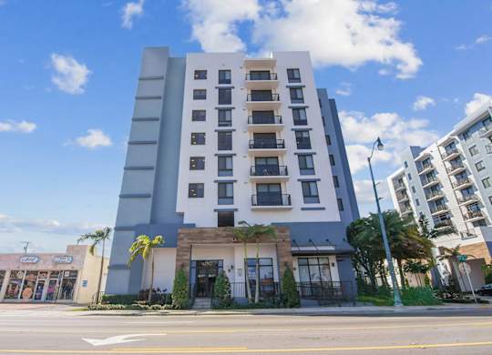 A modern multi-story building with a flat roof and a parking lot in front.