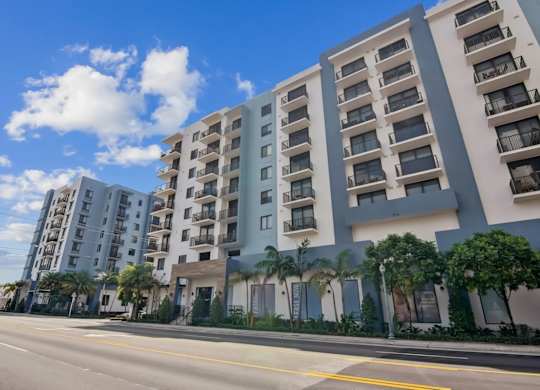 A row of modern apartment buildings with balconies and palm trees in front.