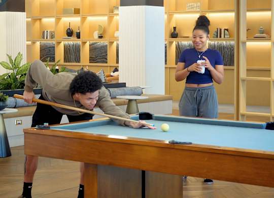 A man is playing pool while a woman watches and drinks coffee at Era Apartments in Denton, TX