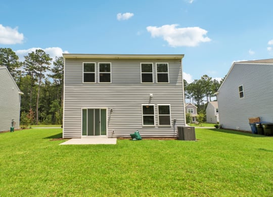 Open grassy area behind the house with clear skies and greenery at Beacon at Ashley River Landing in Summerville, SC