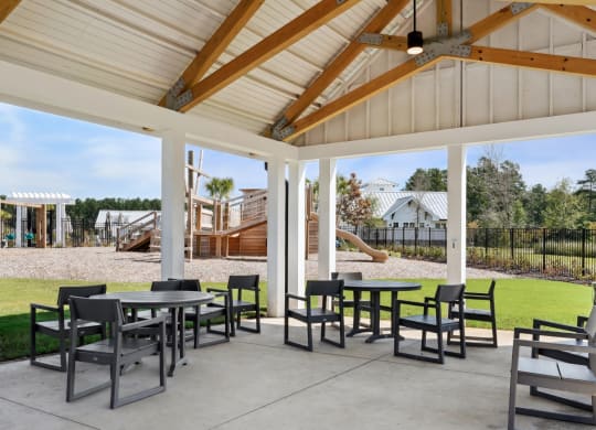 Covered pavilion with tables and chairs and the playground in the background at Beacon at Ashley River Landing in Summerville, SC