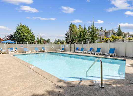 A large swimming pool surrounded by a white fence and blue lounge chairs at Abbey Rowe Apartments in Olympia, WA