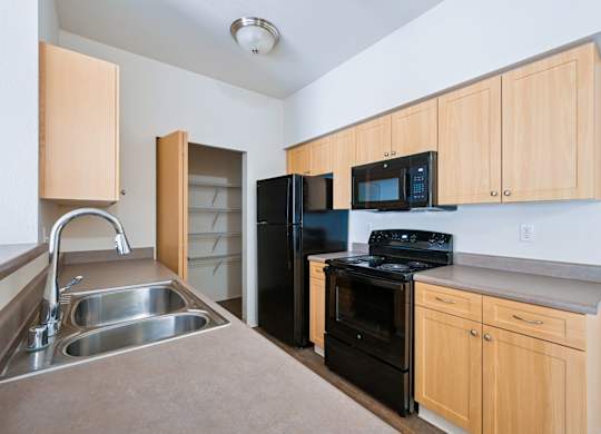Soho kitchen with black appliances, a pantry closet, and wooden cabinets at Abbey Rowe Apartments in Olympia, WA