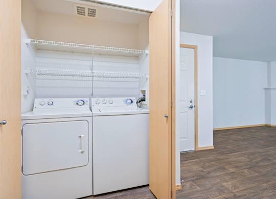 A full size washer and dryer in the York floorplan with the living room in the background at Abbey Rowe Apartments in Olympia, WA