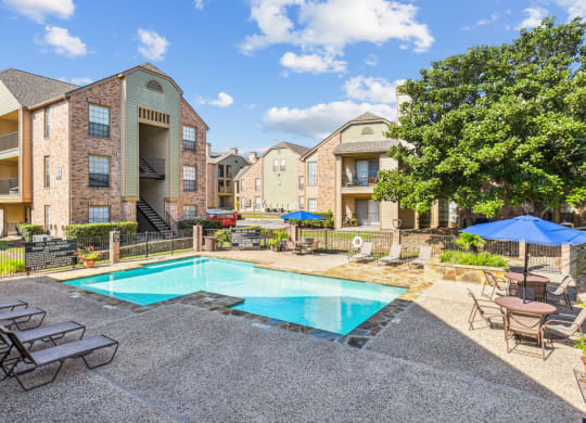 Community pool with lounge chairs surrounded by apartments at Bandera Crossing apartments in San Antonio, TX