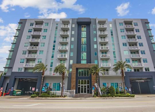 The exterior of a modern, multistory apartment building with a blue sky and clouds in the background at Blue Lagoon 7 Apartments in Miami, FL