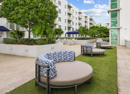 a seating area with tables and chairs on a lawn in front of an apartment building
