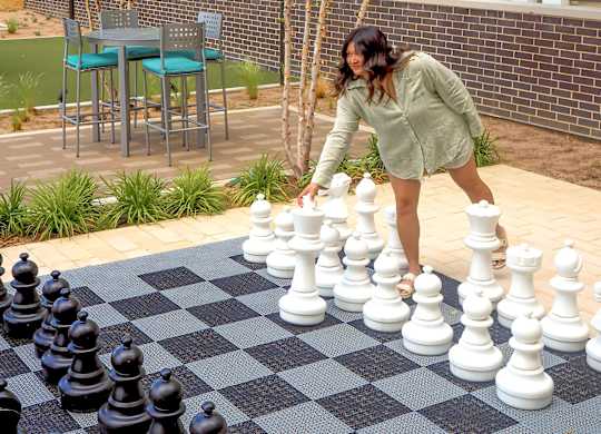 A woman is playing chess on a checkered mat at Era Apartments in Denton, TX