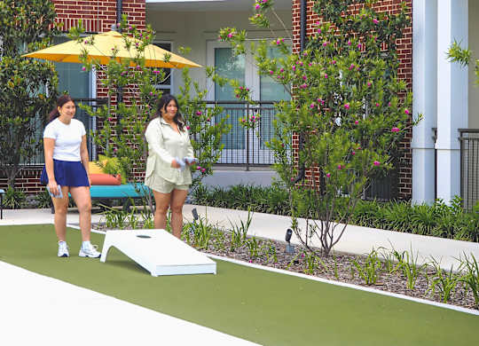 Two women playing cornhole in front of Apartments at Era in Denton TX.