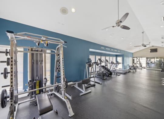 Fitness center with weights and cardio machines, squat rack, and ceiling fans at Davenport Apartments in Dallas, TX
